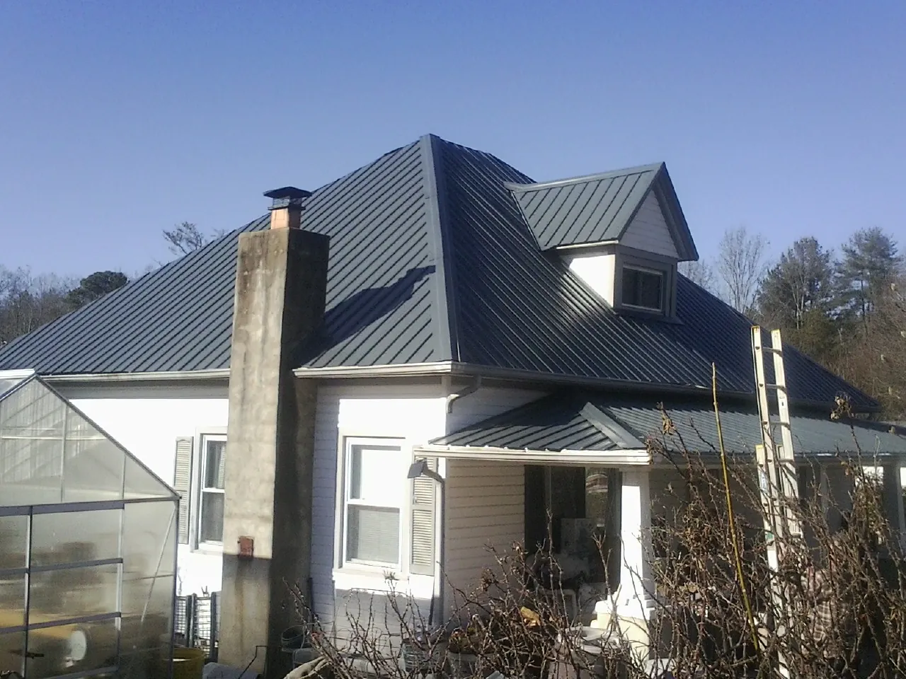 Dark blue standing seam metal roof on a white farmhouse with dormer — Slate & Tile Roof Repair by Roofing Brothers in Haledon