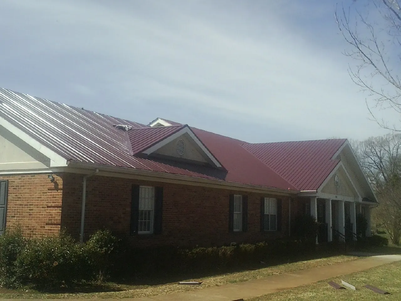 Red metal roof with gabled entries on a long brick building, from a Hail Damage Roof Repair job in Haledon