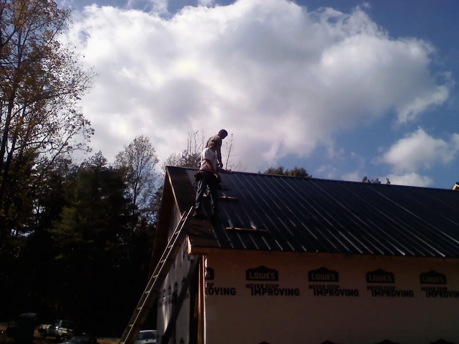 Roofer fastening dark metal panels high against a cloudy sky, from a Roof Inspection job in Haledon