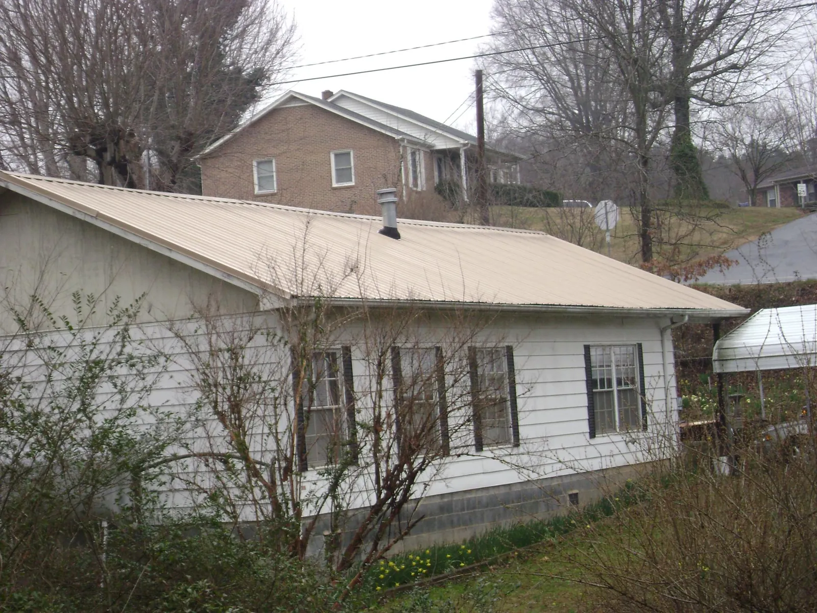 Tan metal roof on a white sided house set into a hillside in Haledon